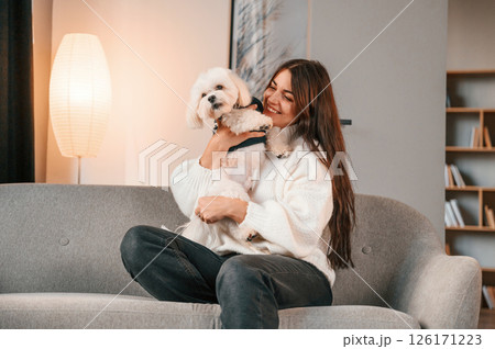 Sitting on the sofa. Beautiful woman is with maltese dog is at home 126171223