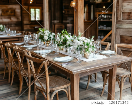 Indoor banquet with long tables, white flowers, candles, plates, and crystal glasses, elegant setting. Indoor banquet with long tables, white flowers, candles, plates, and crystal glasses, elegant setting. 126171343