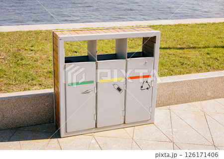 Trash can with three bins sits on a sidewalk next to a body of water. recycling. 126171406