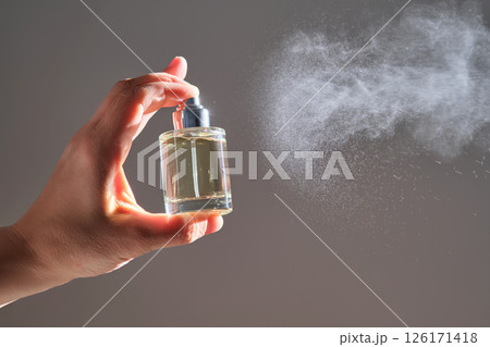 The hand sprays perfume from a transparent rounded bottle. 126171418