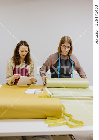 Two female seamstresses and fashion designers stand at table with roll of fabric negotiate 126171453