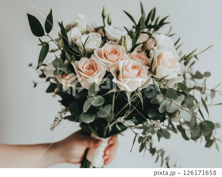 A bouquet of white and pink roses held in a woman's hand on the white background. 126171658