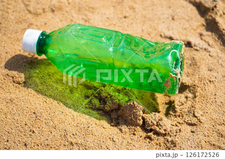 Plastic bottle on sandy beach. Empty uncapped used plastic drinking water bottles piled up with sand, dumped on the beach with copy space. Polluted garbage abandoned by tourists. 126172526
