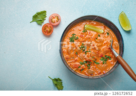 Brazilian traditional dish moqueca de camarao with shrimps, lime, peppers, and cilantro is served in a bowl on light blue background top view, space for text 126172652