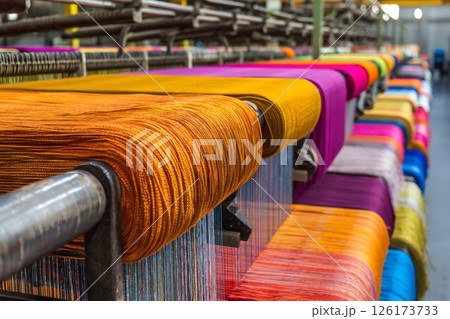 Rows of industrial weaving machines processing colorful threads and producing various fabrics 126173733