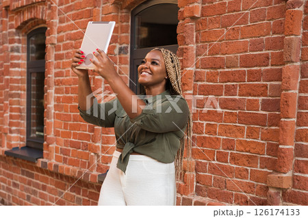 African american woman smiling and holding a tablet while walking on city. Communication, happiness, and digital connection with loved ones 126174133