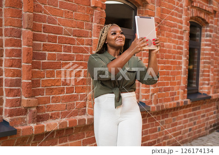 African american woman smiling and holding a tablet while walking on city. Communication, happiness, and digital connection with loved ones African american woman smiling and holding a tablet while walking on city. Communication, happiness, and digital connection with loved ones 126174134