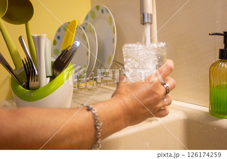 A woman's hand holding a glass with clean water coming out of a faucet A woman's hand holding a glass with clean water coming out of a faucet 126174259