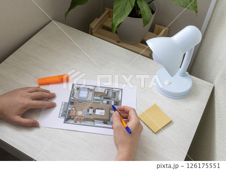 Man studies layout of the small, furnished apartment printed on the sheet of paper placed on the desk 126175551