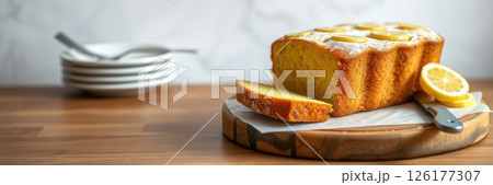 Freshly baked lemon cake on a wooden board with slices and plates ready for serving in a cozy kitchen setting 126177307