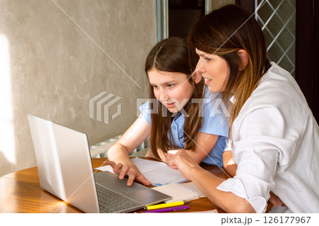 Happy mother with preteen daughter using laptop in home kitchen. Working on school project. Helping with homework using technologies. Happy mother with preteen daughter using laptop in home kitchen. Working on school project. Helping with homework using technologies. 126177967