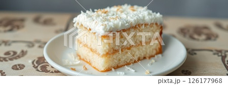 Delicious coconut cake slice on a white plate resting on a decorative table with an inviting backdrop 126177968