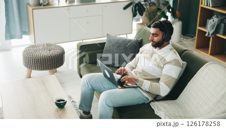 Headphones, man and laptop in home for hybrid work, journalism and research story. Typing, music and freelancer on sofa with computer for streaming audio, writing article and news report on internet 126178258