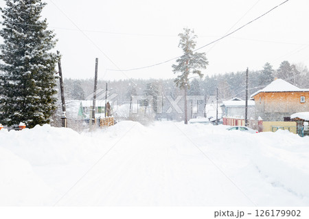 Snow blankets the village street in a quiet rural areas, with homes and tall trees peeking through the falling snowflakes on a winter day. 126179902
