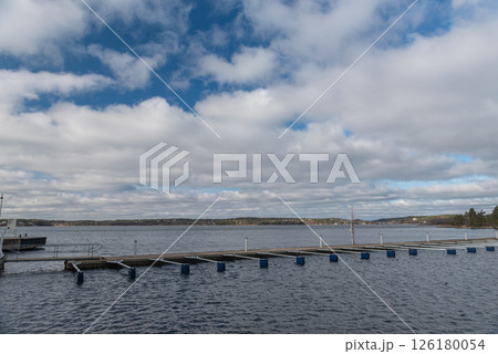 Empty marina for tourist and boating season to start. Early spring view of mooring. landscape with row of free piers on lake. Sunny cloudy day. Empty marina for tourist and boating season to start. Early spring view of mooring. landscape with row of free piers on lake. Sunny cloudy day. 126180054