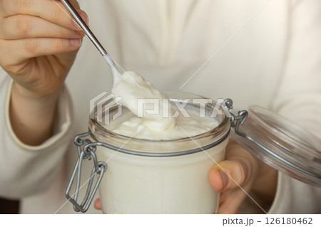 Unrecognizable woman eating from Glass jar natural organic homemade yogurt. Immunity-boosting ingredients. Concept of healthy eating breakfast of Greek yogurt Unrecognizable woman eating from Glass jar natural organic homemade yogurt. Immunity-boosting ingredients. Concept of healthy eating breakfast of Greek yogurt 126180462