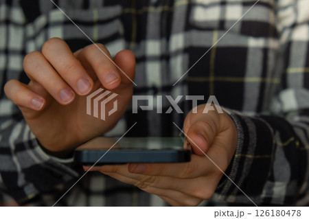 Close-up shot of woman's hands tapping on mobile phone screen. Girl in plaid shirt using modern smart phone. template mock up copy space Close-up shot of woman's hands tapping on mobile phone screen. Girl in plaid shirt using modern smart phone. template mock up copy space 126180478