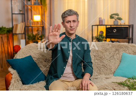 Young man shows stop gesture with raised hand strict face expressing emotional boundary or rejection Young man shows stop gesture with raised hand strict face expressing emotional boundary or rejection 126180637