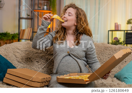 Pregnant woman opening pizza box at home, tasting slice with satisfied smile, enjoying comfort food Pregnant woman opening pizza box at home, tasting slice with satisfied smile, enjoying comfort food 126180649