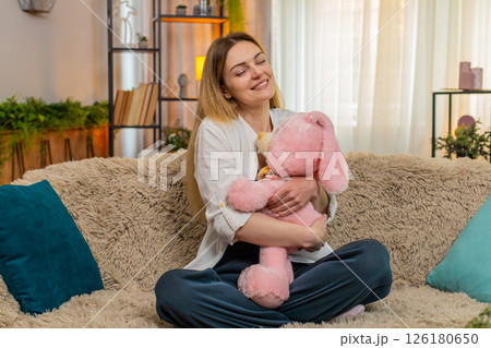 Woman hugging plush toy at home smiling with comfort and calmness feeling safe emotionally grounded Woman hugging plush toy at home smiling with comfort and calmness feeling safe emotionally grounded 126180650