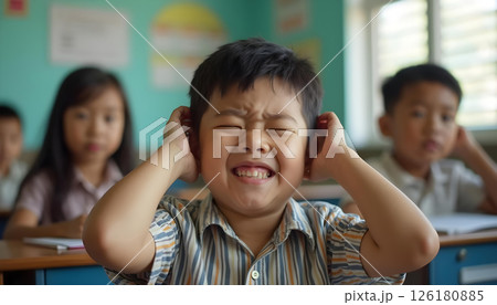Autistic asian boy male child kid covering ears at school classroom. Autism spectrum hypersensitivity, sensory overload, distress, headache, overwhelmed sensory input 126180885