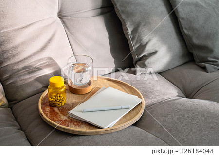 Couch with Tray Holding Medicine Bottle, Glass of Water and Notebook. Daily Routine for Health and Wellness at Home. Couch with Tray Holding Medicine Bottle, Glass of Water and Notebook. Daily Routine for Health and Wellness at Home. 126184048