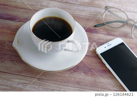 スマートフォンと木製のテーブルの上に置かれたコーヒーと眼鏡 126184621