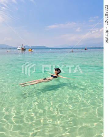 A brunette Russian girl in a black swimsuit and cap relaxes on Nha Trang beach. Sunny day, South China Sea, Vietnam. A brunette Russian girl in a black swimsuit and cap relaxes on Nha Trang beach. Sunny day, South China Sea, Vietnam. 126185822