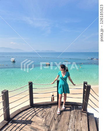 Russian tourist in blue dress enjoying Vietnam beach vacation. Aerial view from pier showing crystal clear water and white sand in Nha Trang. Russian tourist in blue dress enjoying Vietnam beach vacation. Aerial view from pier showing crystal clear water and white sand in Nha Trang. 126185823