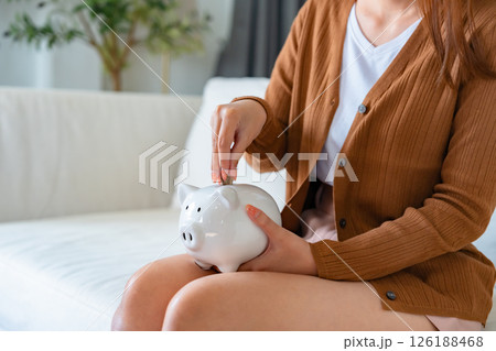 Young Asian woman holding piggy bank and sitting on the floor at home 126188468