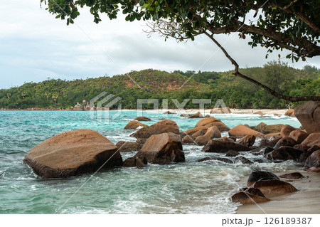 Granite boulders and turquoise water along a tropical beach on Seychelles island, lush green hills 126189387