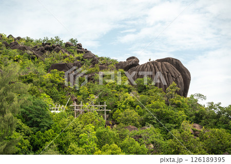 Massive granite rocks surrounded by lush tropical forest under a bright sky on a Seychelles island Massive granite rocks surrounded by lush tropical forest under a bright sky on a Seychelles island 126189395