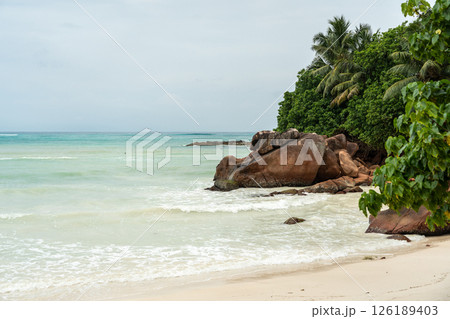 Tropical coast of Seychelles before rain, with cloudy sky, gentle waves, rocky islet 126189403