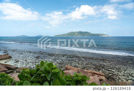 View of granite coastal rocks and ocean waves with distant islands on the horizon under cloudy View of granite coastal rocks and ocean waves with distant islands on the horizon under cloudy 126189418