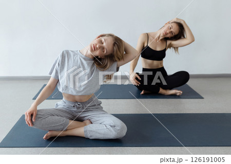 Two athletic attractive girls sit in lotus position on yoga mat indoors .Yoga, fitness and healthy lifestyle Two athletic attractive girls sit in lotus position on yoga mat indoors .Yoga, fitness and healthy lifestyle 126191005