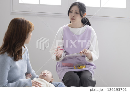 赤ちゃんを抱くお母さんと保健師さん 126193791