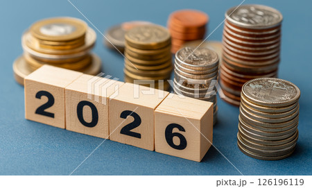 Wooden block with number 2026 alongside stacks of various coins on a blue backdrop Wooden block with number 2026 alongside stacks of various coins on a blue backdrop 126196119