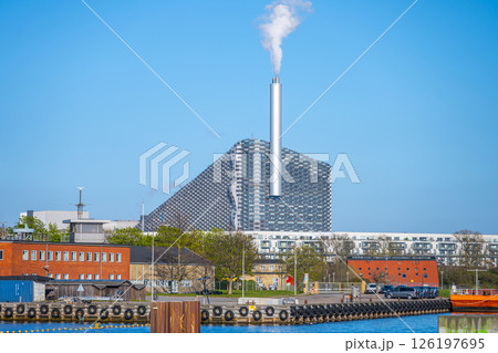 This striking waste-to-energy plant in Copenhagen features a sloped roof for recreation and a chimney emitting steam. It symbolizes sustainable energy and urban innovation. 126197695