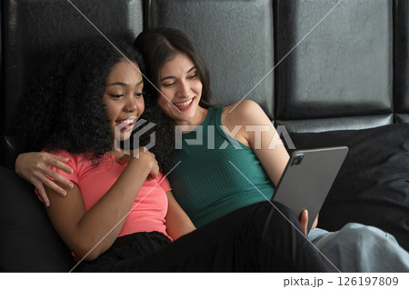 Happy young woman in green cloth that hug her smiling couple while lying on bed and using tablet pc together at home relaxing on weekend morning Happy young woman in green cloth that hug her smiling couple while lying on bed and using tablet pc together at home relaxing on weekend morning 126197809