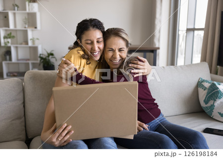 Excited mature mum teen daughter hugging on sofa opening parcel 126198184