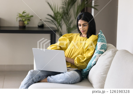 Happy young woman working remotely sitting on couch with notebook Happy young woman working remotely sitting on couch with notebook 126198328