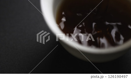 Gently pouring a rich liquid into a beautifully crafted white cup resting on a dark surface. Media Gently pouring a rich liquid into a beautifully crafted white cup resting on a dark surface. Media 126198497