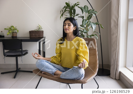 Peaceful young lady meditate sitting on armchair in lotus position 126198529