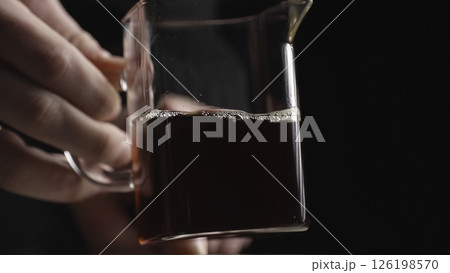 A Close Up View of a Glass Pitcher Holding a Dark Beverage Set Against a Black Background. Media 126198570