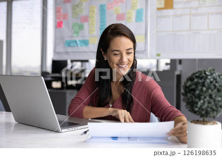 Smiling successful young businesswoman read papers at office work desk 126198635