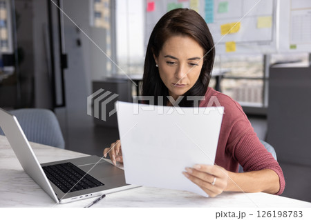 Serious young businesswoman review paper documents before typing on notebook 126198783