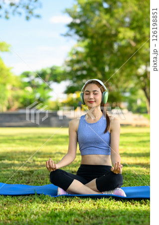 fit woman doing yoga and listening to music on headphones in the park 126198851