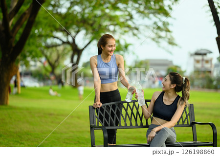 Fit women in sportswear hydrating and relaxing on bench after a workout outdoors 126198860