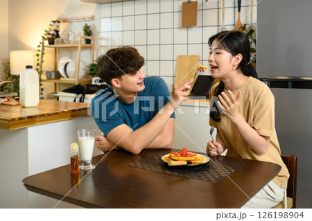Happy couple enjoying homemade pancakes together at breakfast table 126198904