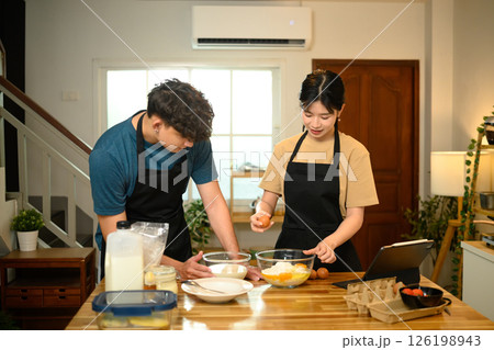Young couple cracking egg into flour while preparing pancake batter together 126198943